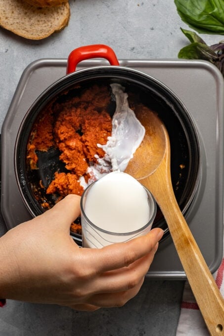 Woman hand pouring milk into the tomato flavored roux.