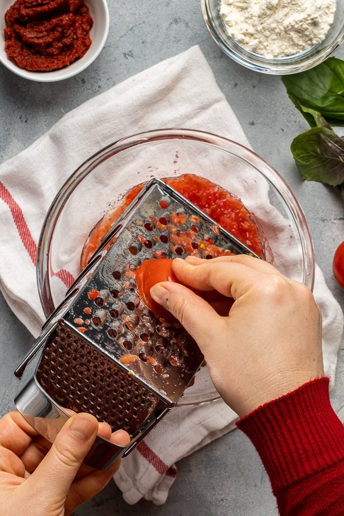 Woman hands grating tomatoes to make soup.