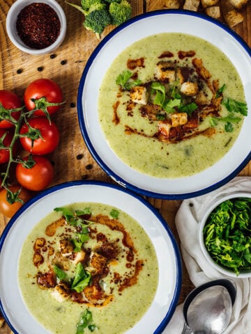 Cream of broccoli soup served in two white bowls on a wooden board.