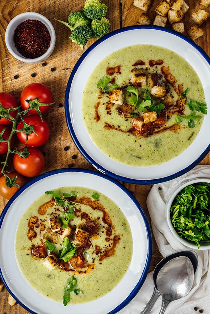 Cream of broccoli soup served in two white bowls on a wooden board.