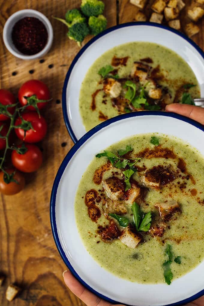 Cream of Broccoli Soup is super creamy without cream. This is such a heart-warming and tasty soup. Ready in less than 30 minutes. Perfect for busy winter days! Someone holding a bowl of cream of broccoli soup