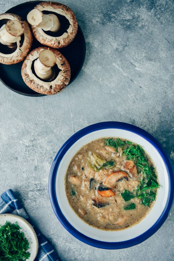 Vegan cream of mushroom soup in bowls and mushrooms accompany.