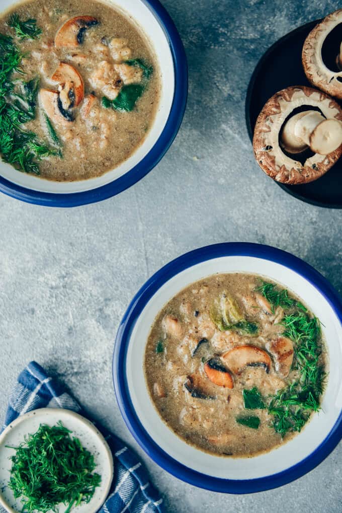 Vegan cream of mushroom soup in bowls and mushrooms accompany.