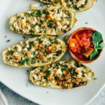 Cheese stuffed zucchini boats served with a hot chili sauce on a white plate