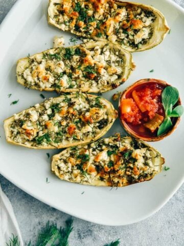 Cheese stuffed zucchini boats served with a hot chili sauce on a white plate