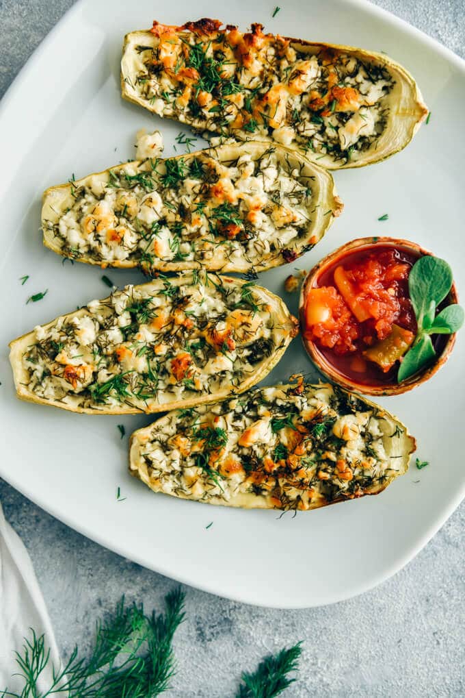 Cheese stuffed zucchini boats served with a hot chili sauce on a white plate