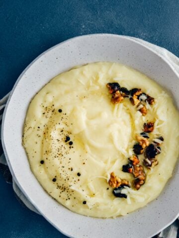 Cheesy mashed potatoes with roasted walnuts and black pepper in a white ceramic bowl.