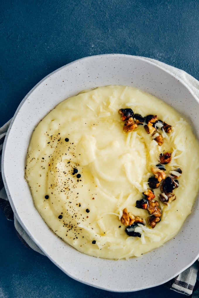 Cheesy mashed potatoes with roasted walnuts and black pepper in a white ceramic bowl.