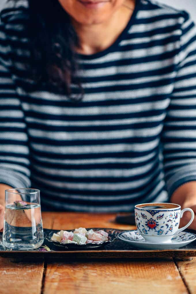 Woman serving Turkish coffee with Turkish delights and a small glass of water on the side on a copper tray.