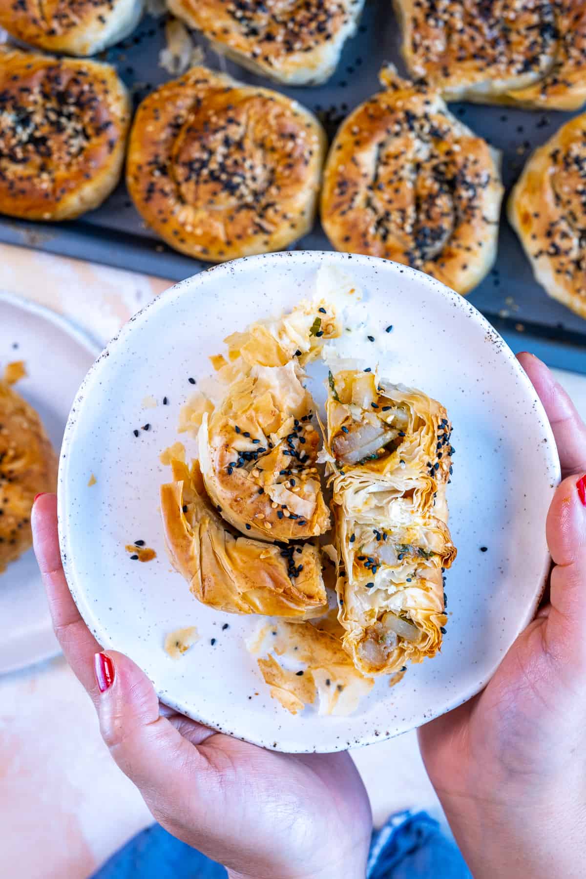 Hands holding halved potato borek on a white plate.