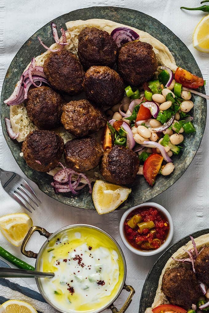 Homemade Turkish Meatballs are spicy, tender and perfectly juicy. It’s not a secret any more to make meatballs at home. #turkishfood #meatballs #meatballsrecipe #middleeasternfood #kofta #kofte Turkish Meatballs served with bean salad on a copper plate and yogurt cucumber dip on the side.