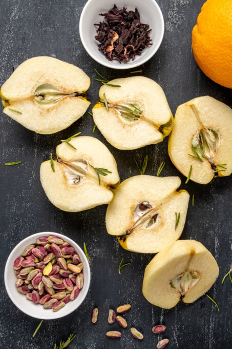 Peeled and halved quince fruit, pistachios, hibiscus leaves and orange on a dark background.