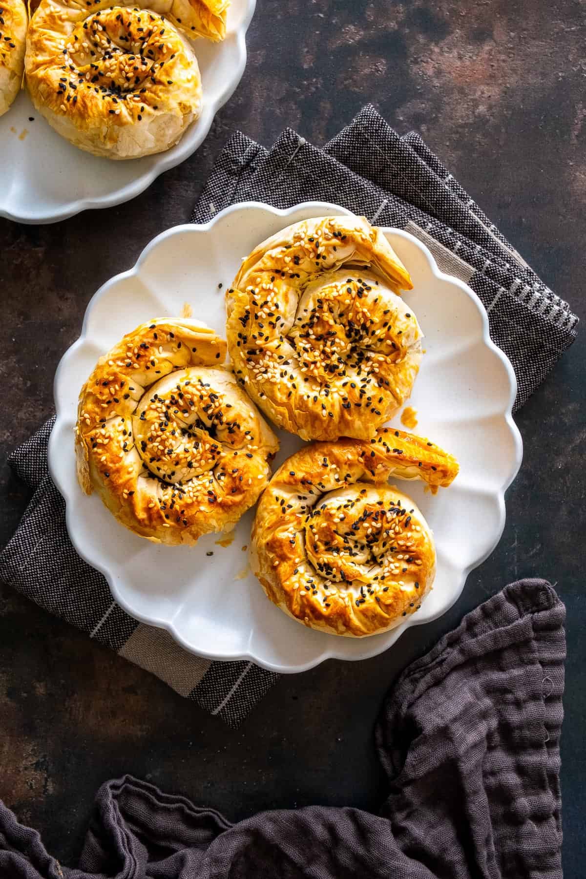 Close-up of three golden spiral potato böreks topped with sesame and nigella seeds on a white plate.