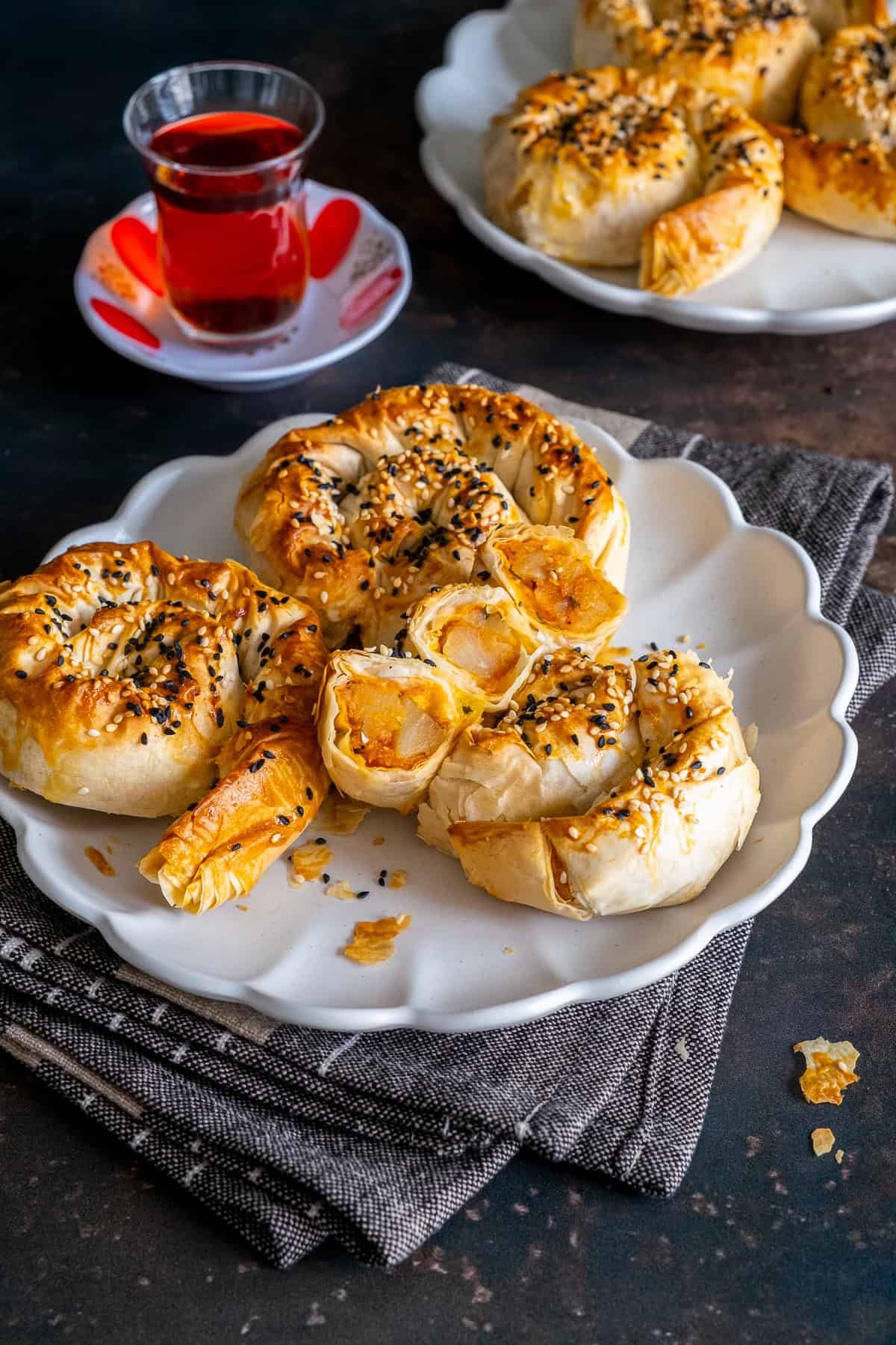 Plate of spiral potato böreks, one cut open to show the potato filling, served with a glass of Turkish tea.