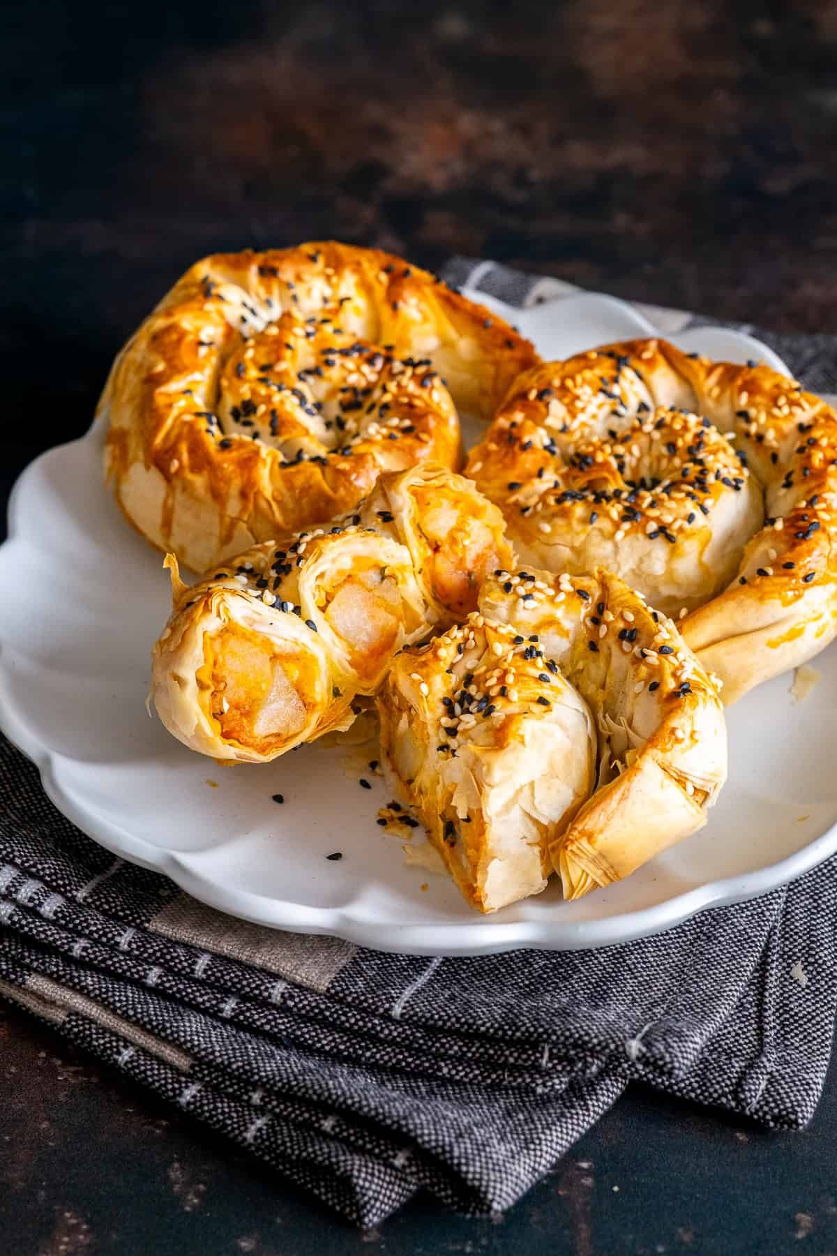 Close-up of spiral potato böreks on a white plate, one cut open to show the golden potato filling.