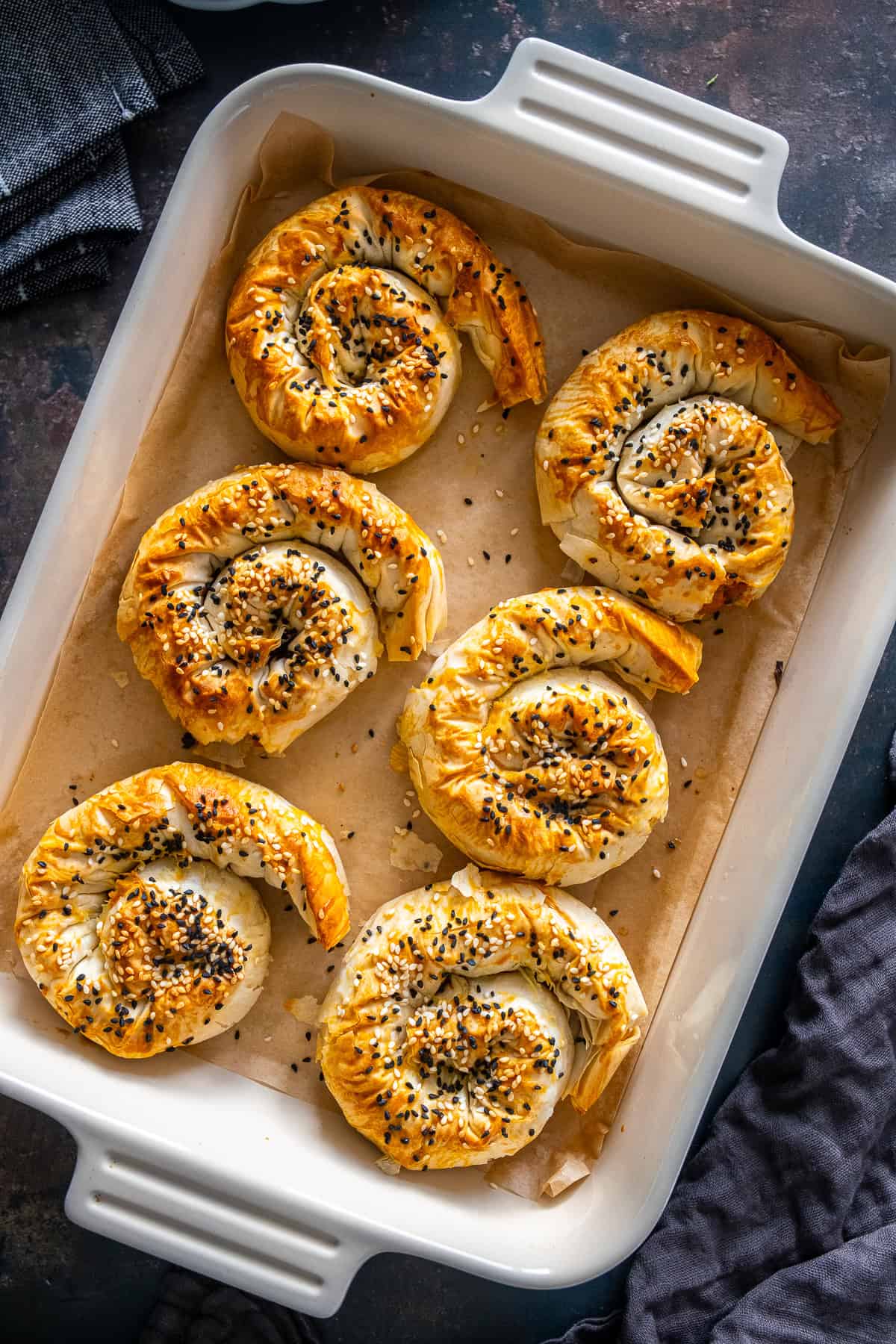 Baking dish filled with golden spiral potato böreks topped with sesame and nigella seeds.