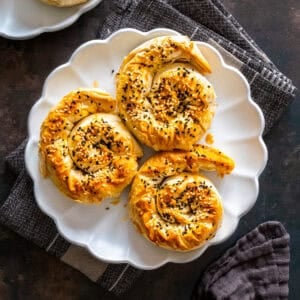Top view of three spiral potato böreks topped with sesame and nigella seeds on a white plate.