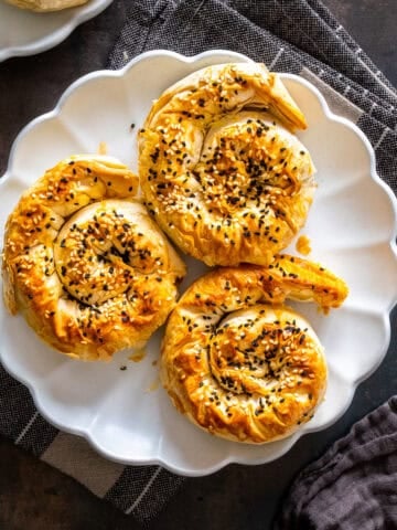 Top view of three spiral potato böreks topped with sesame and nigella seeds on a white plate.