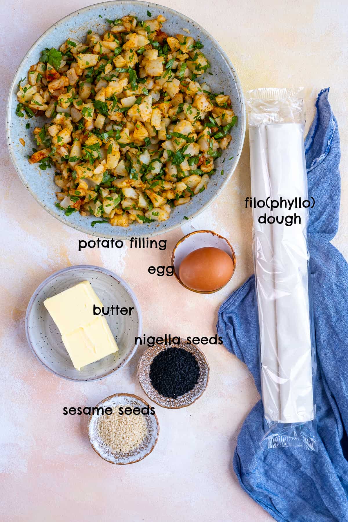 Potato filling, filo pastry, egg, butter, sesame seeds and nigella seeds on a light background.