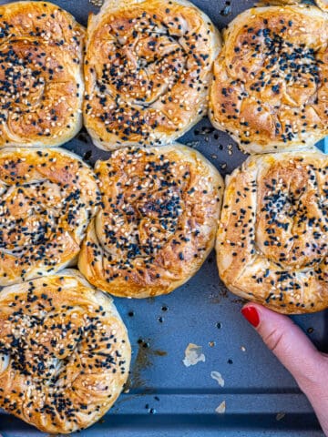 Turkish borek rolls on a baking sheet and a hand is taking one.