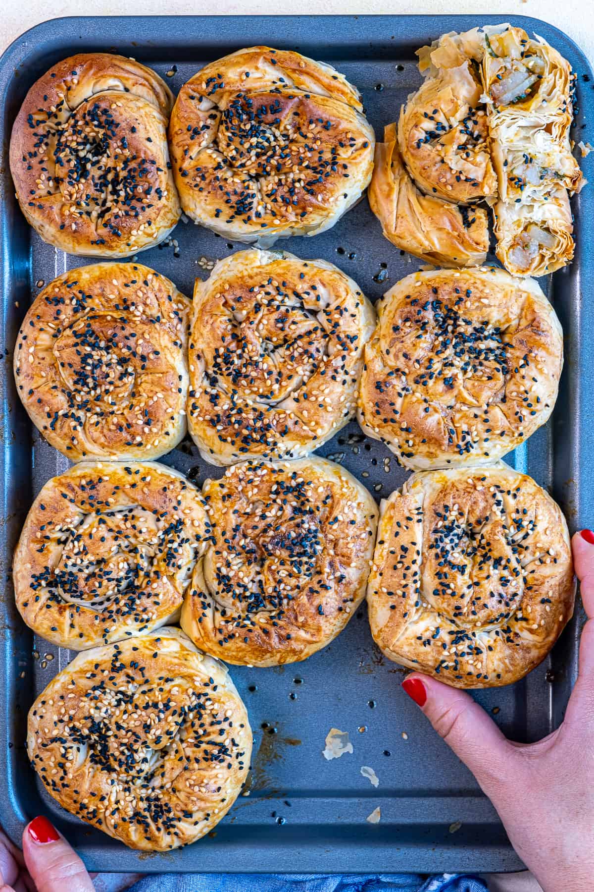 A hand grabbing a roll of potato borek from a baking sheet.