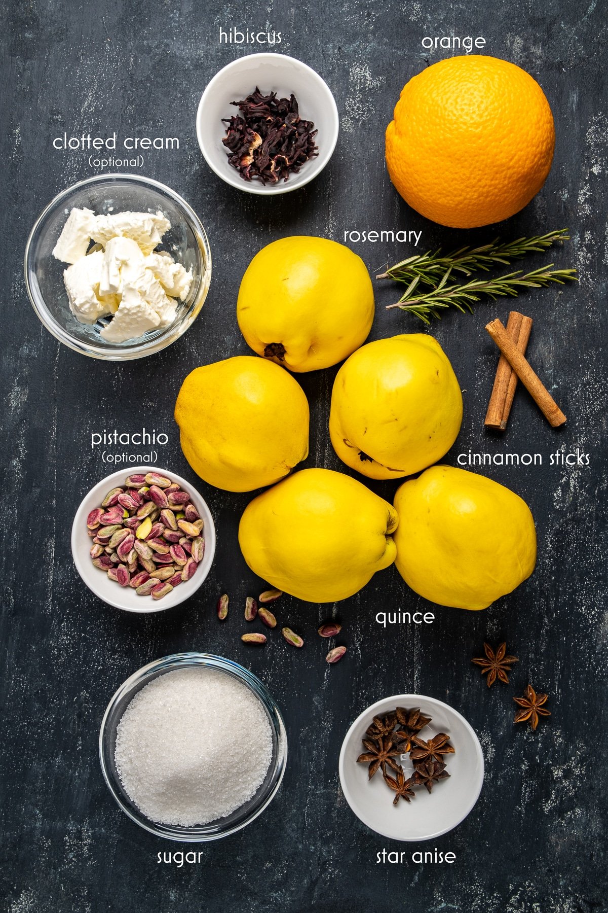 Quinces, cinnamon sticks, rosemary sprigs, orange, sugar, pistachio, hibiscus, star anise, clotted cream are all on a dark background.