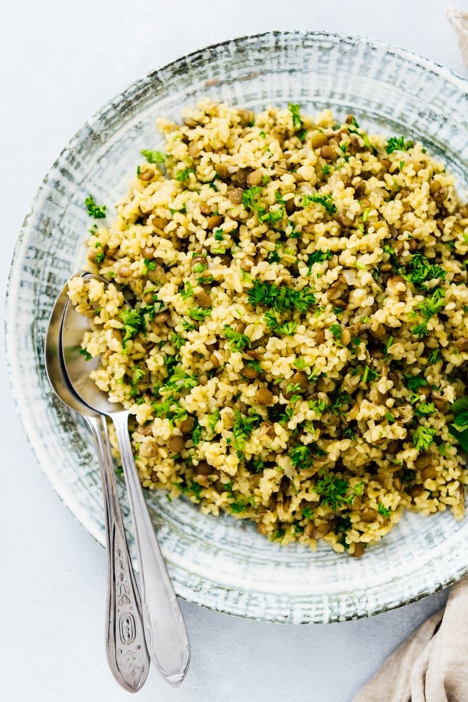 Bulgur pilaf with green lentils and herbs served in a large ceramic bowl.