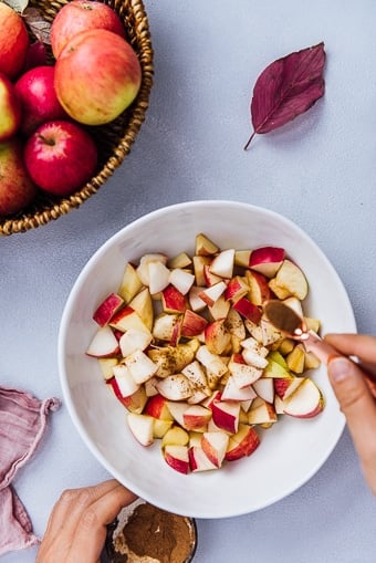 Woman sprinkling cinnamon over diced apples