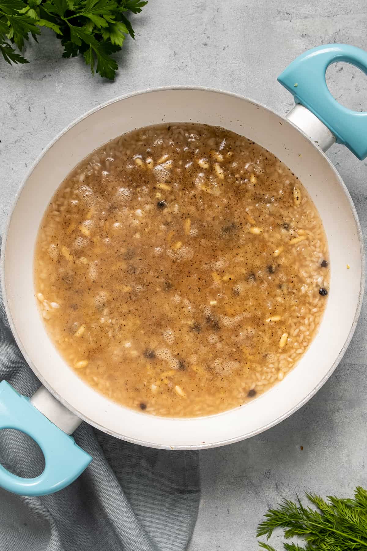 Onions, pine nuts, rice, spices and currants cooking with water in a white pan.