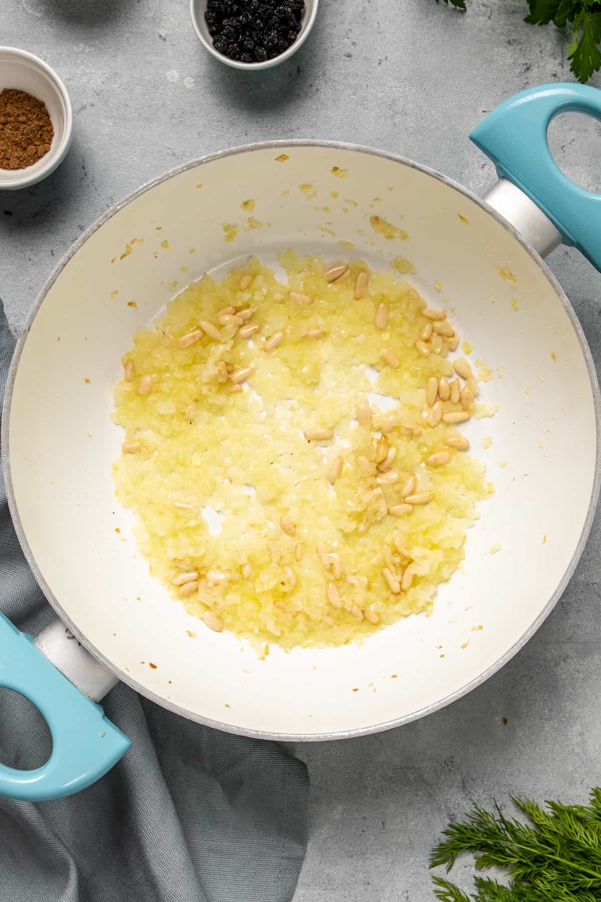 Onions and pine nuts cooking in a white pan.