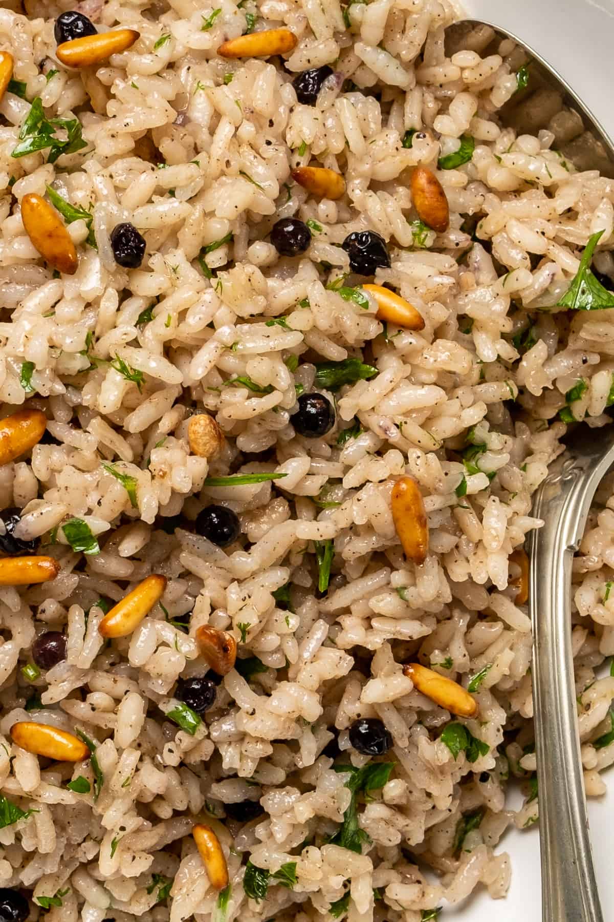 Allspice rice pilaf with raisins, pine nuts and parsley and a spoon in it.