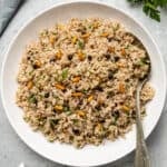 Rice with raisins, pine nuts and herbs in a white bowl and a spoon inside it.