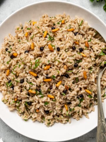 Rice with raisins, pine nuts and herbs in a white bowl and a spoon inside it.