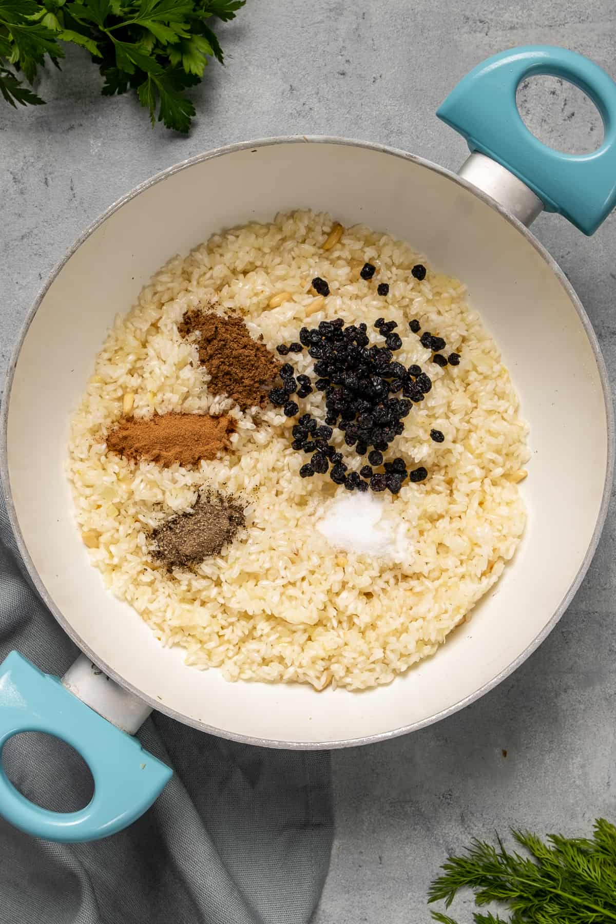 Rice, currant raisins, allspice, cinnamon, salt and pepper in a white pan.