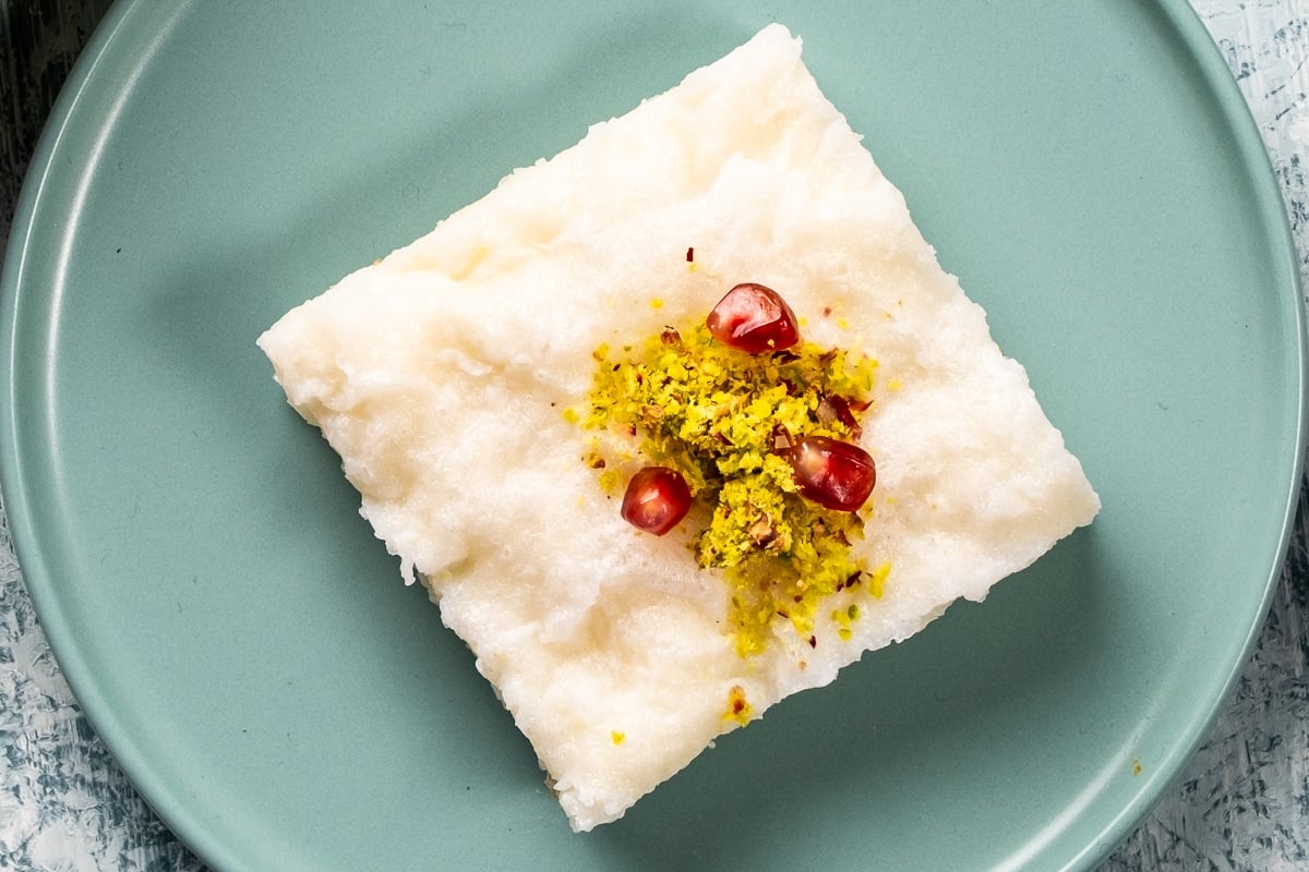 A slice of gullac dessert topped with ground pistachio and pomegranate arils.