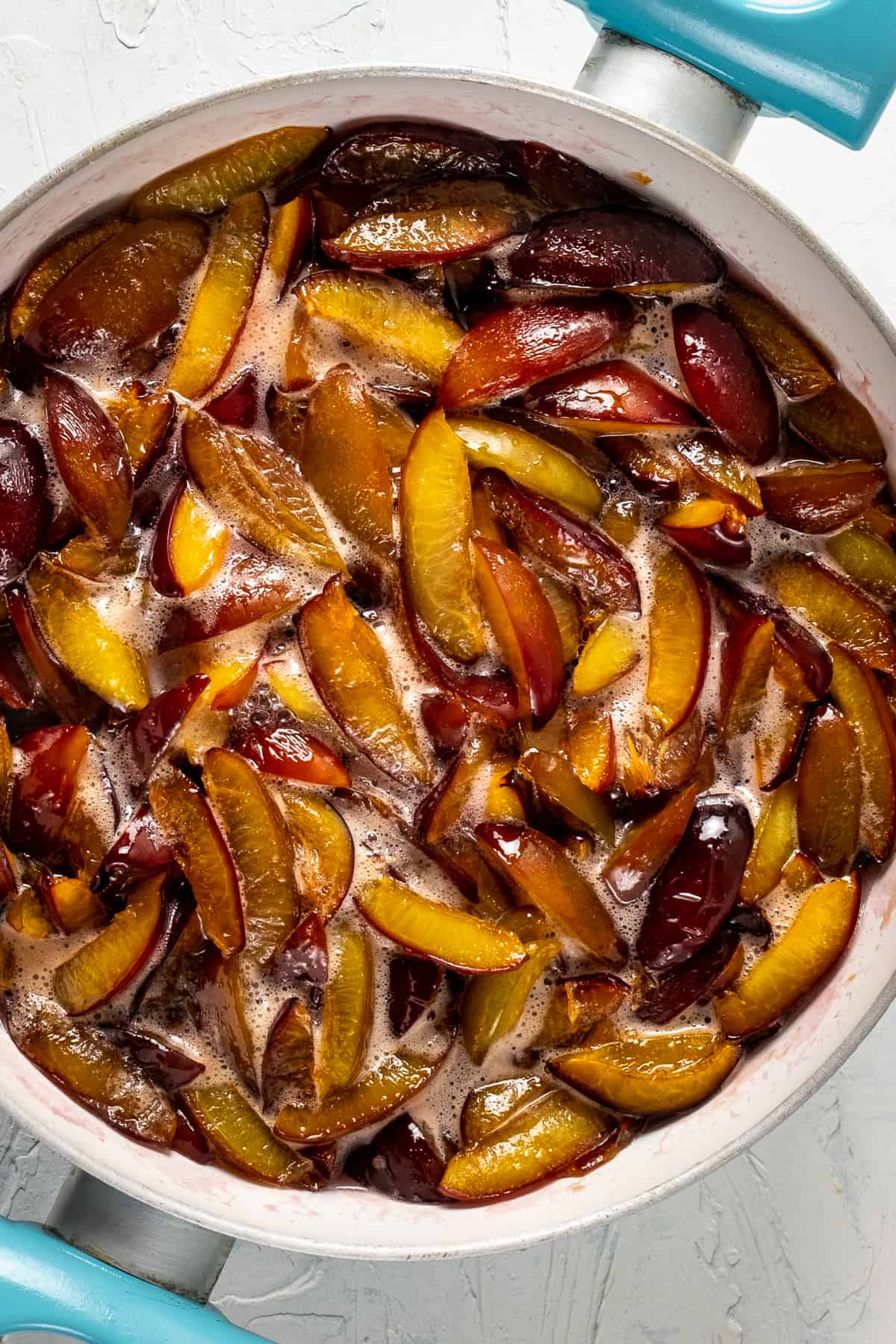 Jam with sliced damson plums cooking in a white bottomed pan.