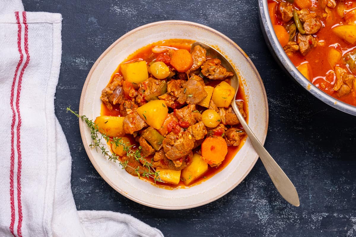 Lamb stew with potatoes and carrots in a large bowl and a spoon in it. Another dish with stew on the side.