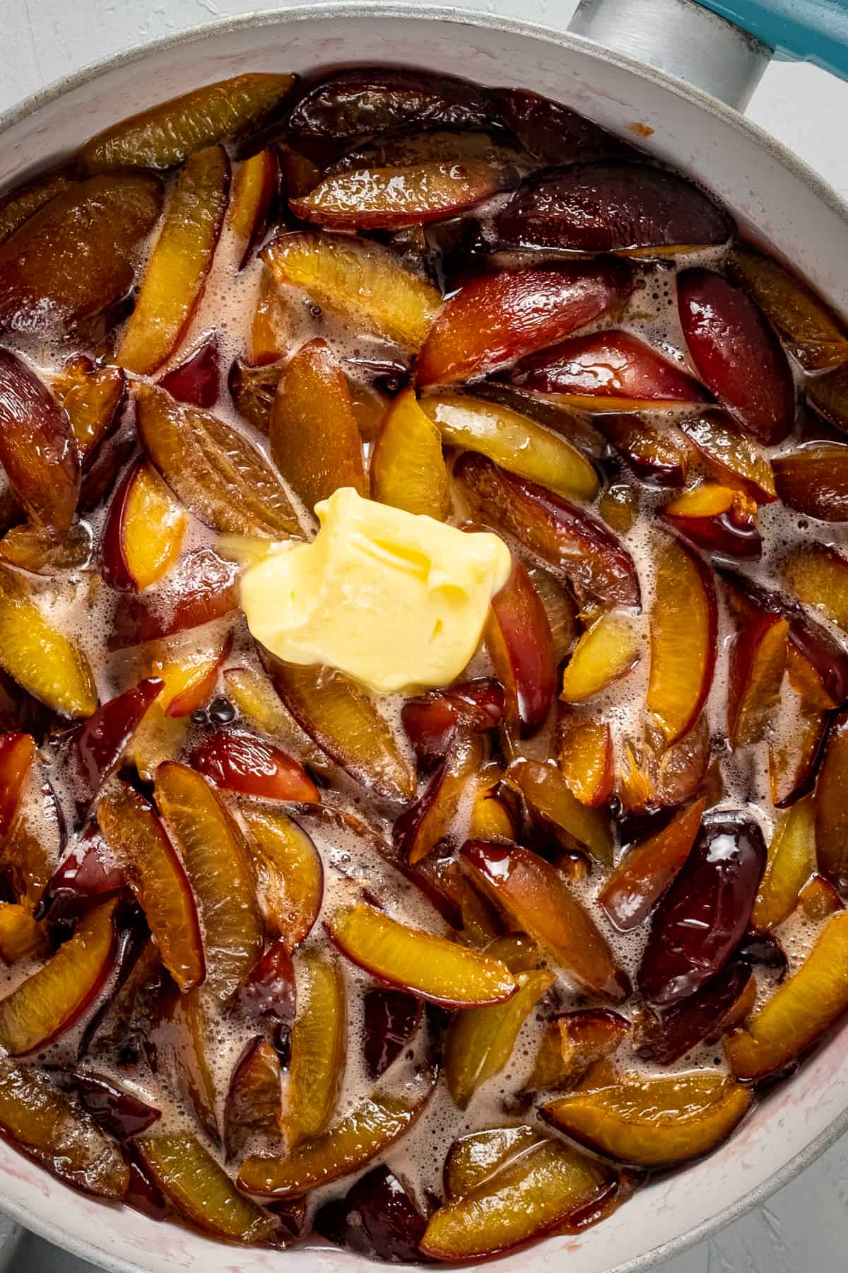 Chunky plum jam cooking with a dollop of butter in a pan.