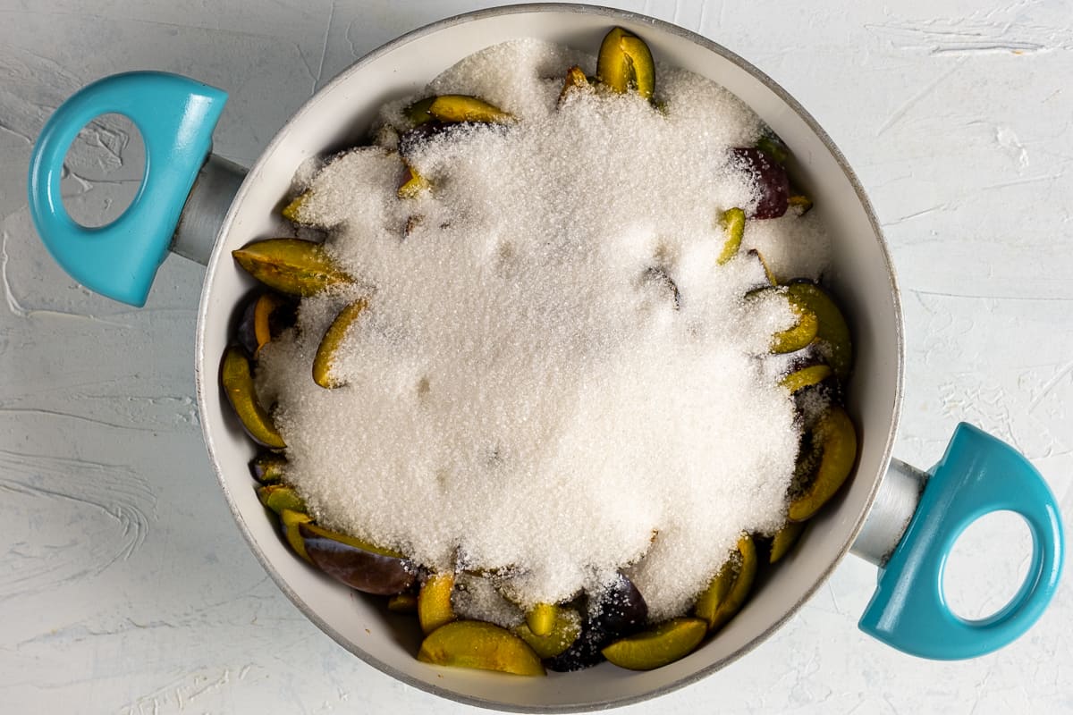 Sliced plums covered with granulated sugar in a white pan.