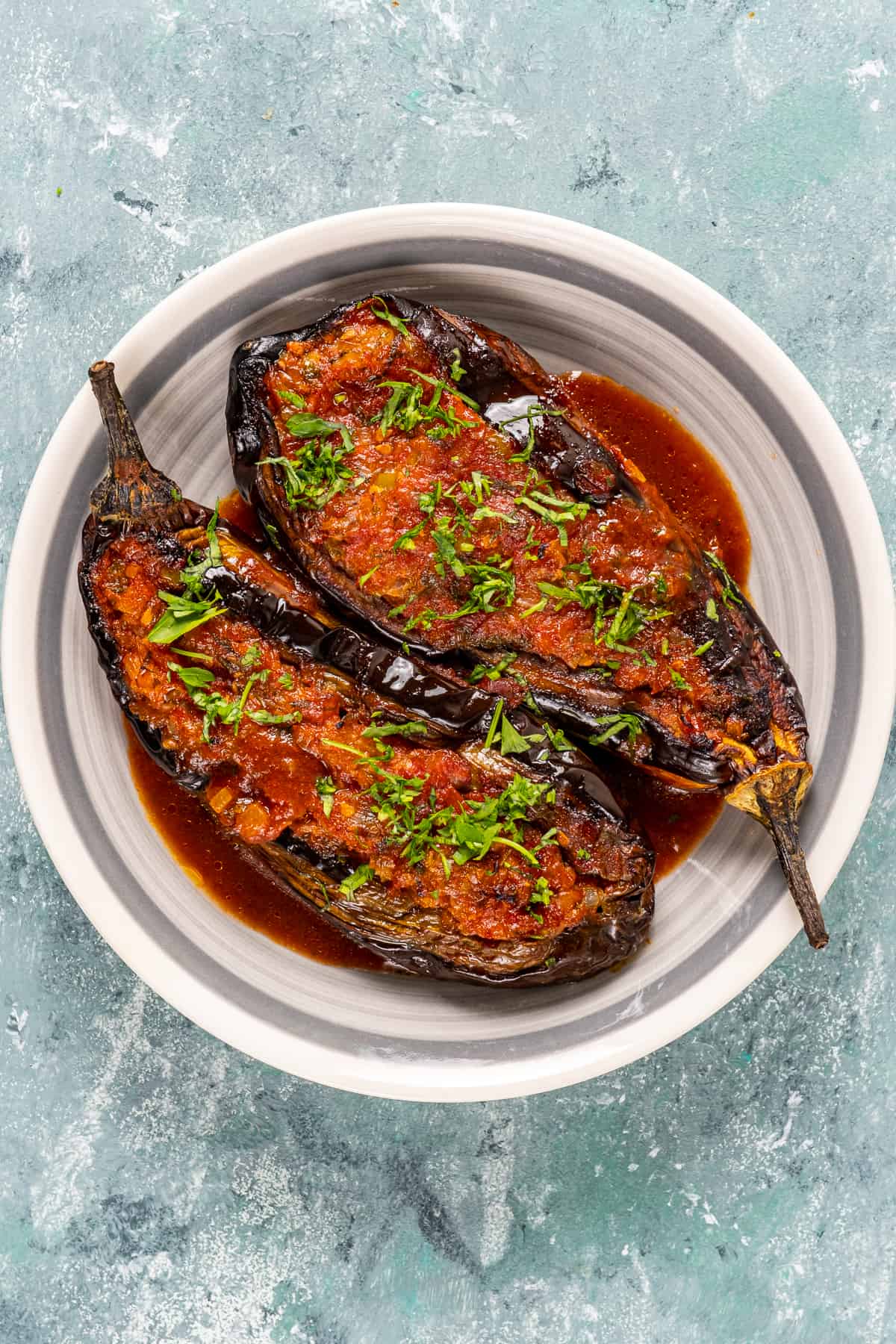 Stuffed roasted eggplants topped with tomato sauce and herbs in a white dish.