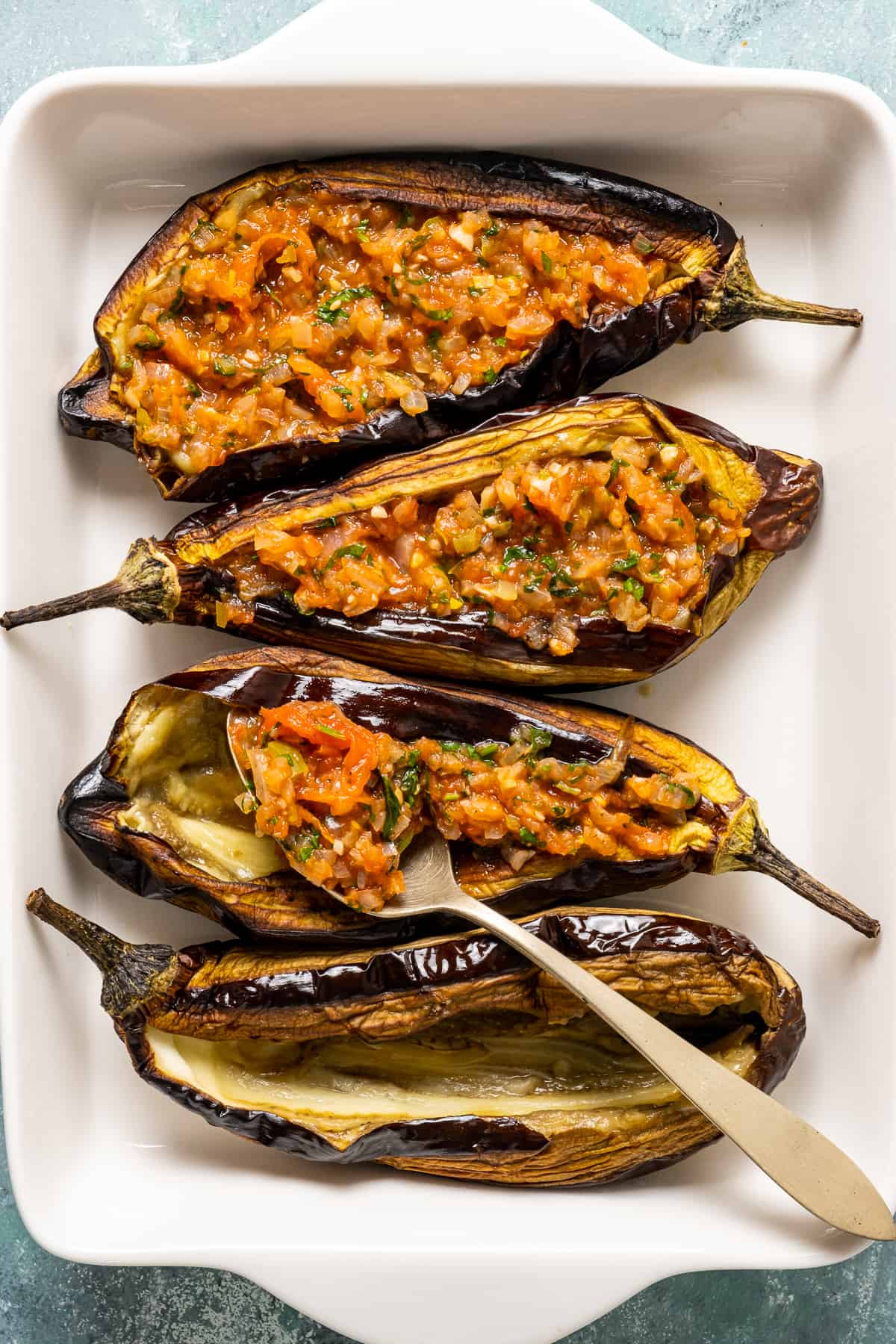 Stuffing roasted eggplants with tomato and onion filling with a spoon.