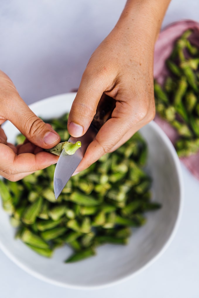 Hands preparing okra for cooking by removing their stems.