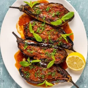 Imambayildi topped with tomato sauce and herbs served in a white oval dish.