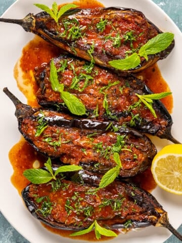 Imambayildi topped with tomato sauce and herbs served in a white oval dish.