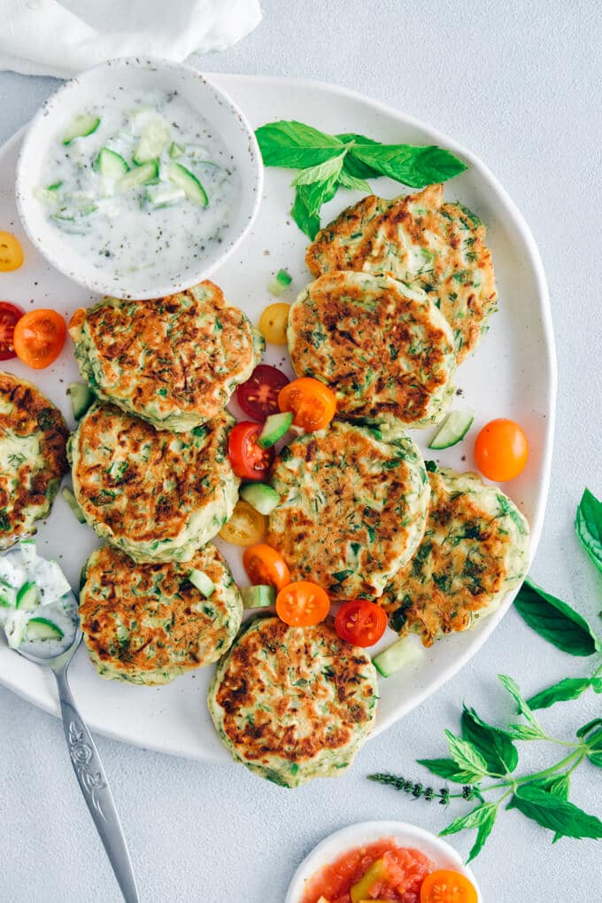 Zucchini fritters on a ceramic plate served with grape tomatoes and yogurt dip