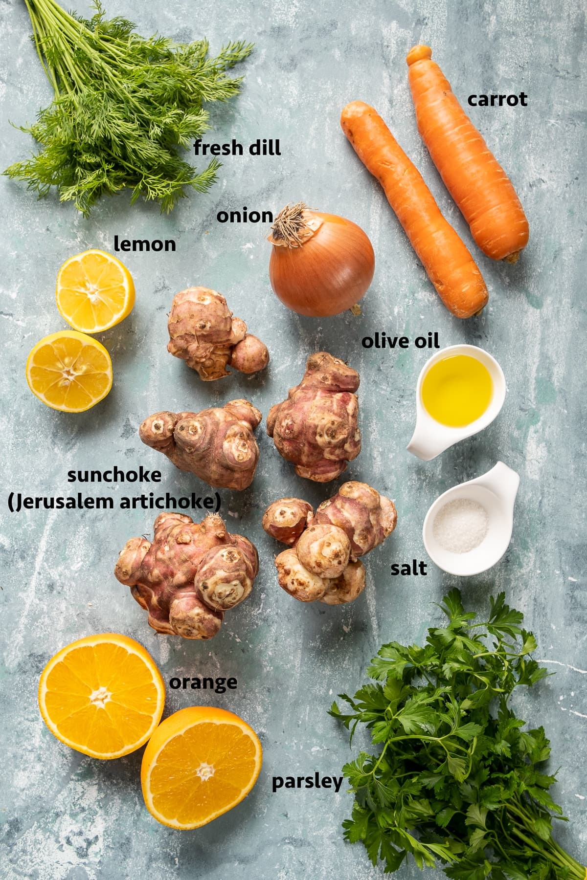 Sunchokes, carrots, onion, halved lemon, halved orange, olive oil, salt, fresh dill and fresh parsley on a light colored background.