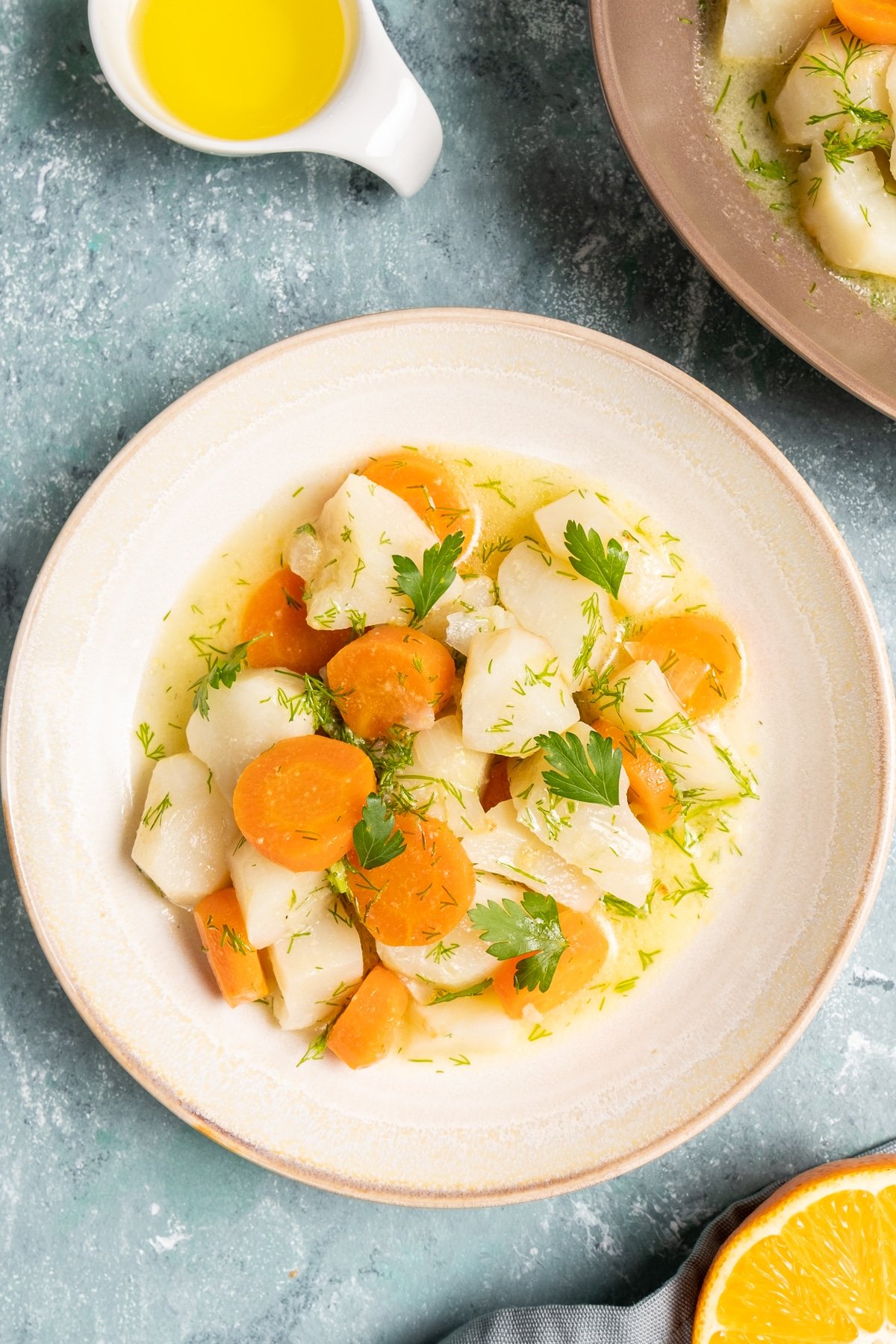 Vegetarian sunchoke dish with carrots garnished with herbs in a white round plate. A slice of orange and olive oil on the side.