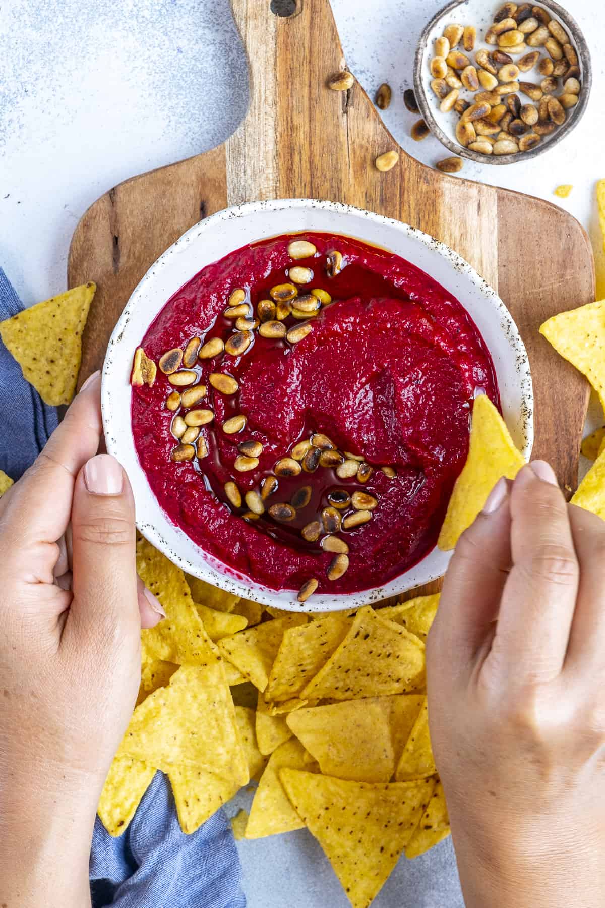 Hands dipping chips into beetroot dip.