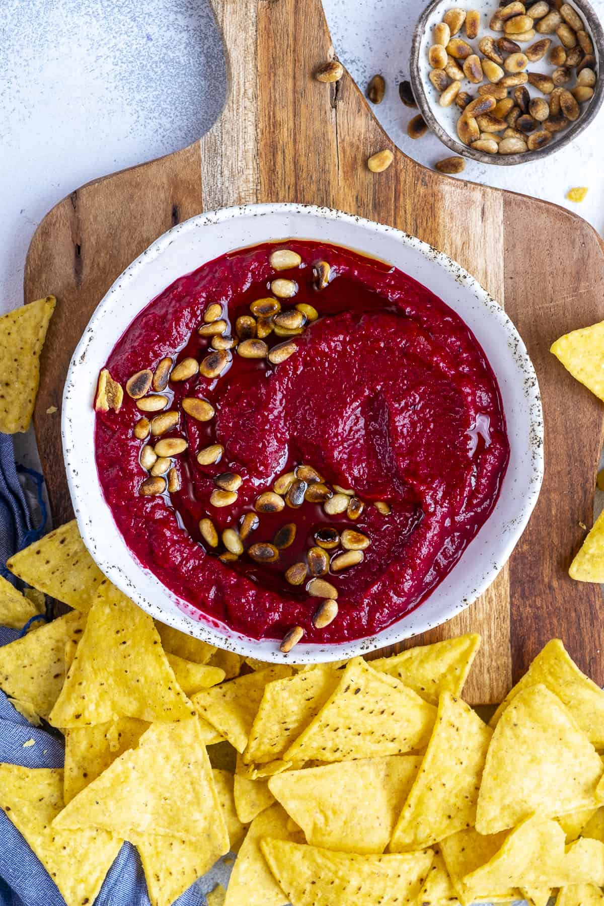 Beetroot dip garnished with pine nuts in a bowl served on a wooden board with chips.