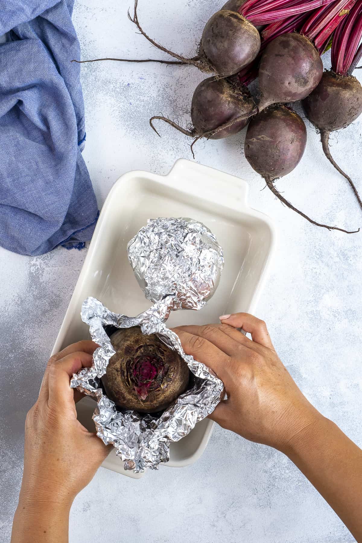 Hands wrapping beets with foil in a baking pan.